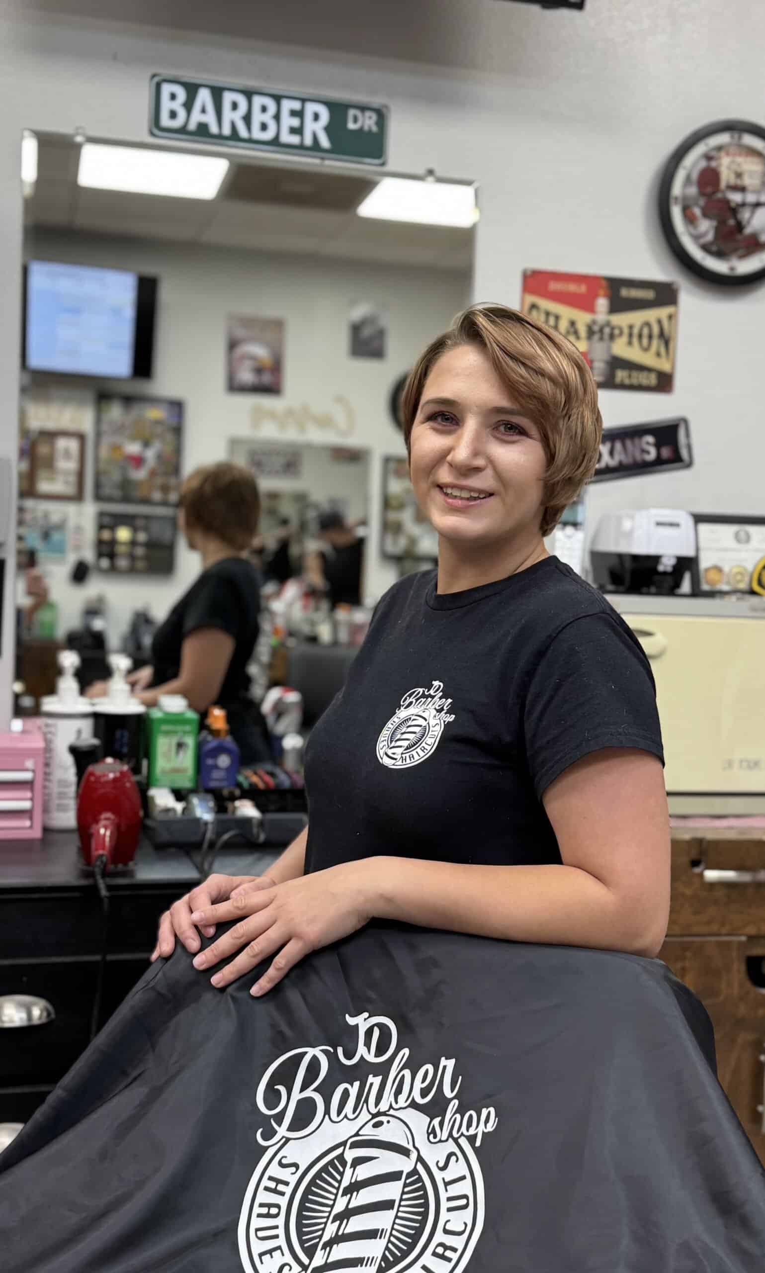 Penny Smiling young woman at JD Barber Shop getting a haircut in a modern barbershop setting.